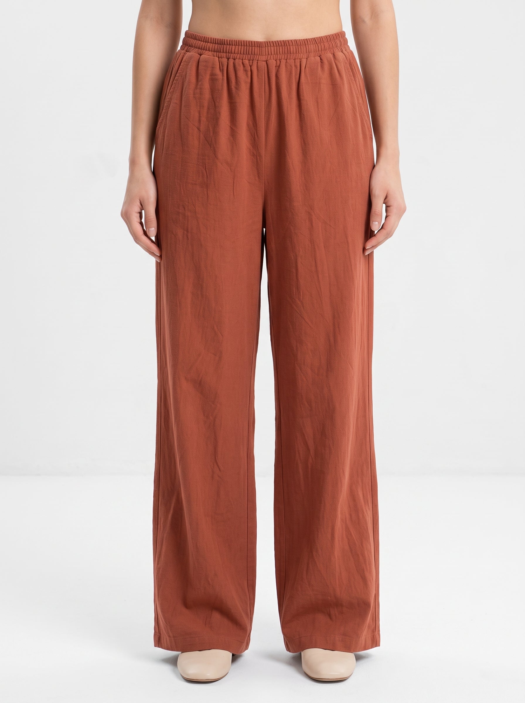 Studio photo of Pantalón rojizo Lower body shot from waist down, facing camera, showing pants/skirt front, legs straight. CAMERA SHOT: A FULL BODY shot capturing the person from head to toe. [Upper body focus]