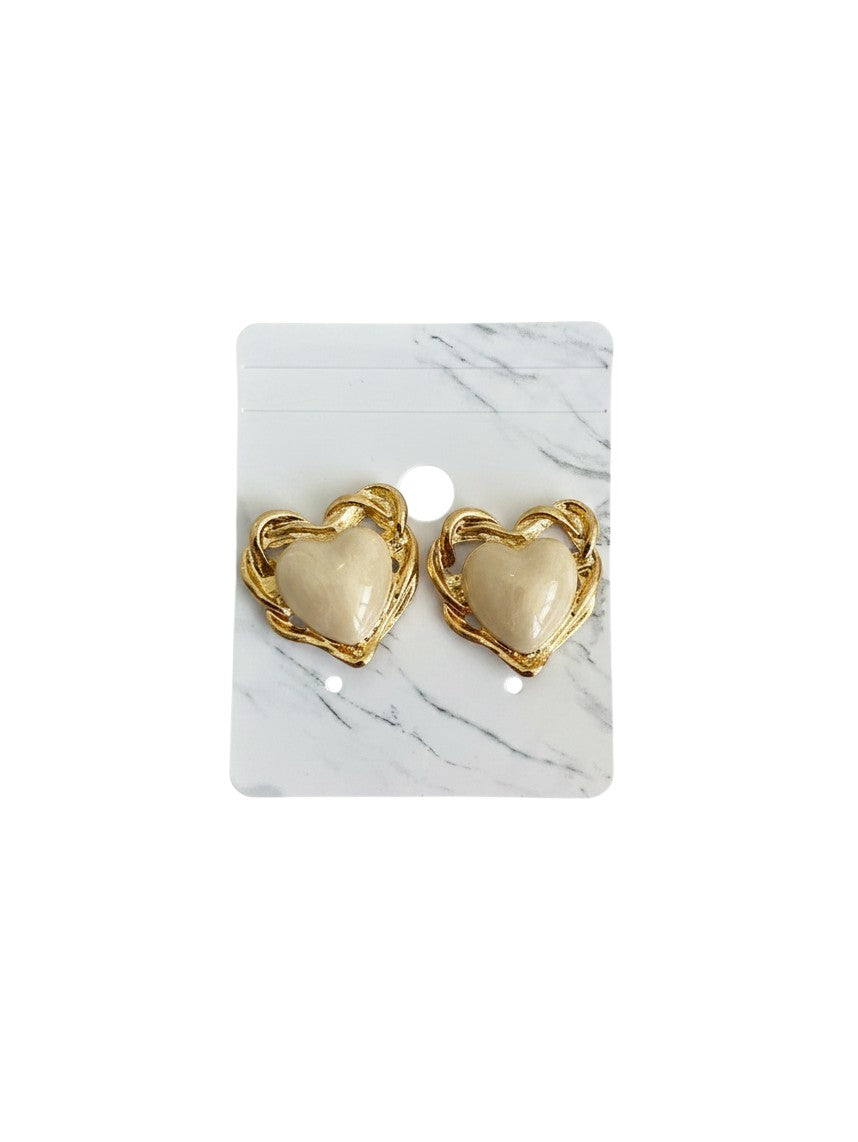 Yanet Collective heart-shaped stud earrings with cream centers and gold-toned twisted metal frames on a marble card.