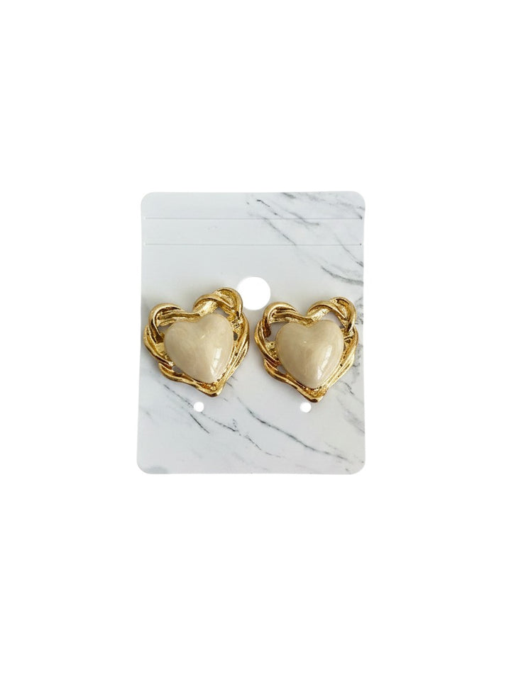 Yanet Collective heart-shaped stud earrings with cream centers and gold-toned twisted metal frames on a marble card.