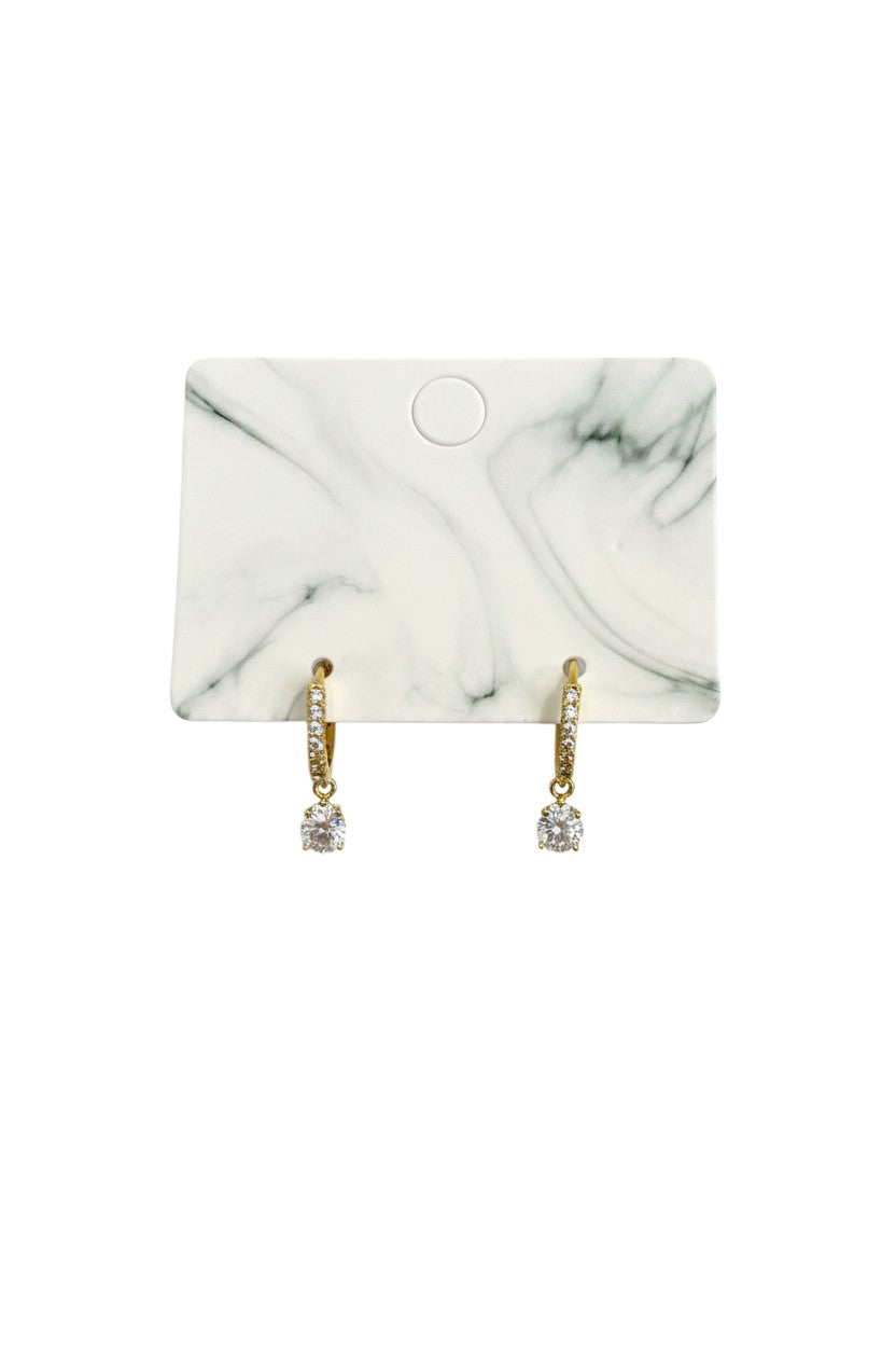 Yanet Collective gold hoop earrings with a dangling round crystal drop on a marble display card