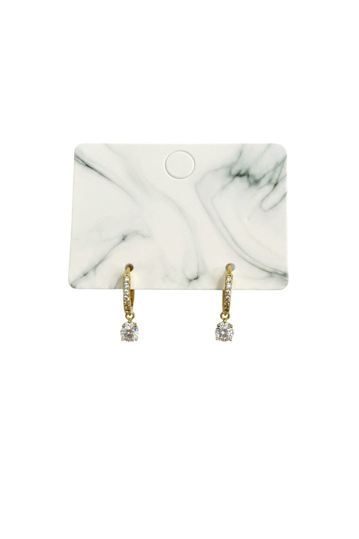 Yanet Collective gold hoop earrings with a dangling round crystal drop on a marble display card
