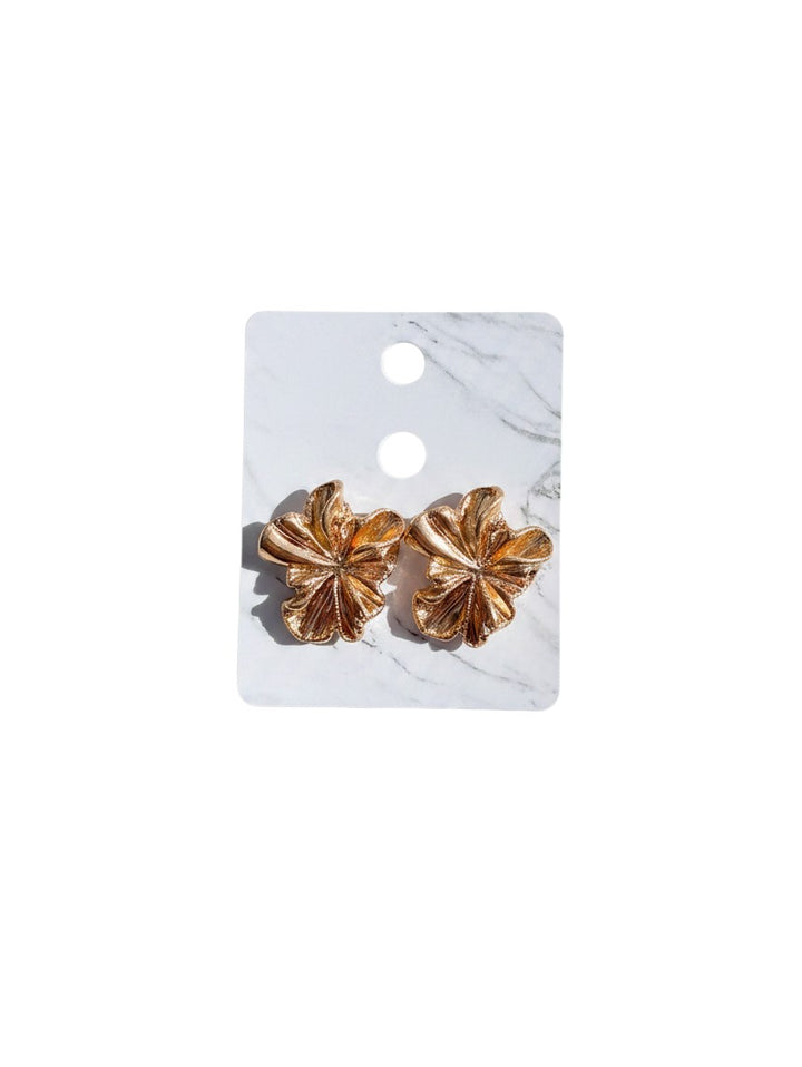 Yanet Collective gold flower-shaped stud earrings with a textured metallic finish on a white marble display card