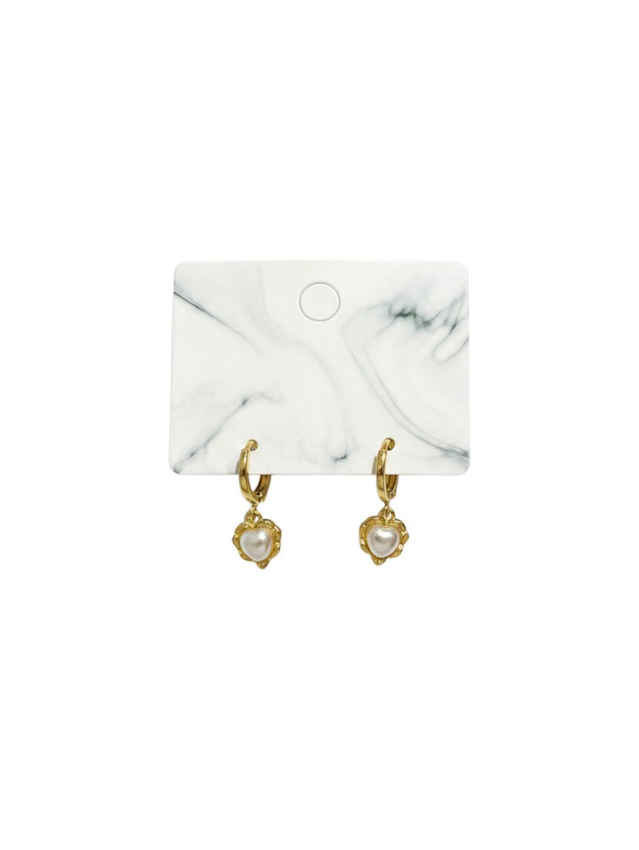 Yanet Collective gold hoop earrings featuring small heart-shaped charms with central white pearls on a marble display card