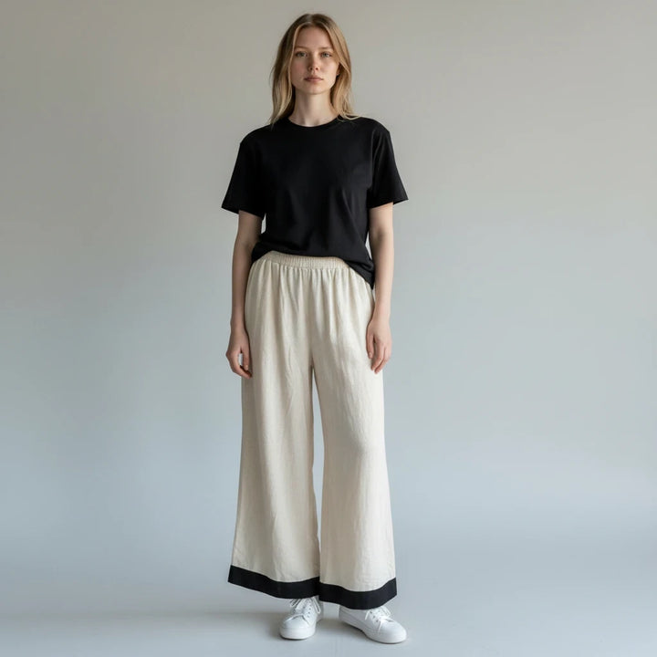 Modelo vistiendo pantalones Yanet Collective beige wide-leg con ribete negro y camiseta negra sobre fondo neutro