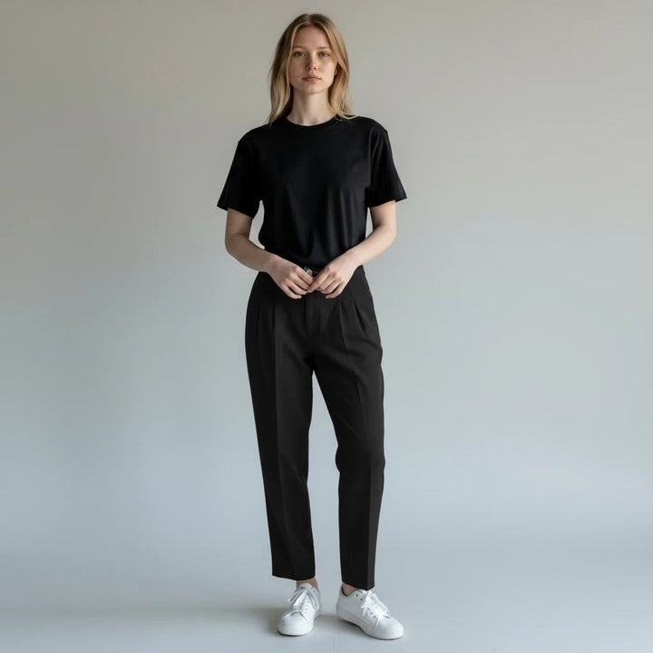 Modelo vistiendo pantalones negros plisados de Yanet Collective con camiseta negra y zapatillas blancas